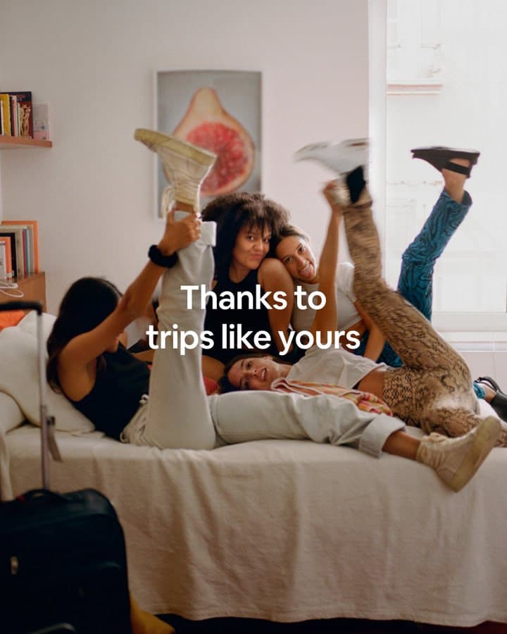 Friends laughing on a bed with their legs in the air. Caption: Thanks to trips like yours.